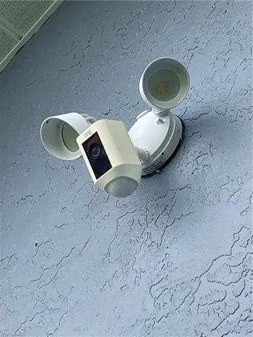 Exterior wall-mounted security camera with integrated floodlights, featuring a textured stucco finish