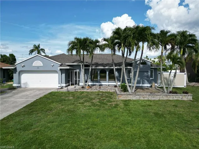 Contemporary stucco exterior featuring a two-car garage, multiple palm trees, a stone-faced raised planter, and an arched window design