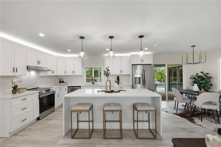 Kitchen featuring stainless steel appliances, hanging light fixtures, white cabinets, a kitchen island, and light hardwood / wood-style floors