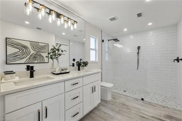 Bathroom with tiled shower, wood-type flooring, double vanity, and toilet