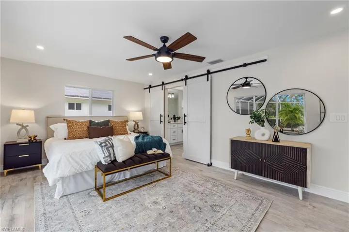 Bedroom with multiple windows, light wood-type flooring, connected bathroom, and a barn door