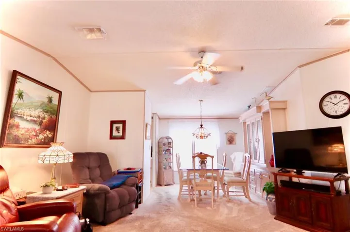 Living area featuring light carpet, crown molding, a ceiling fan, and a textured ceiling