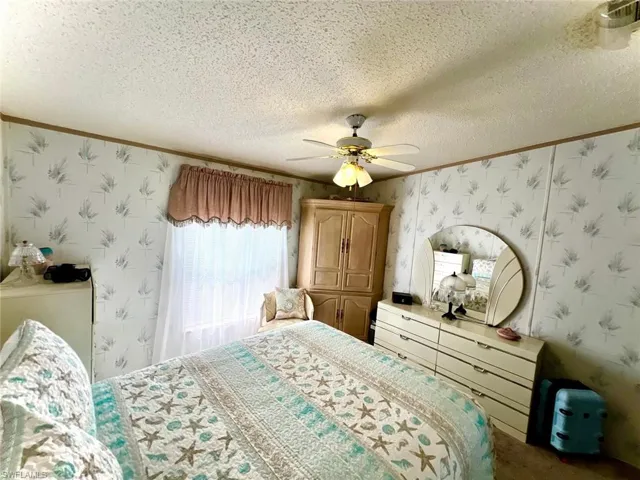 Bedroom with wallpapered walls, ornamental molding, a textured ceiling, and ceiling fan