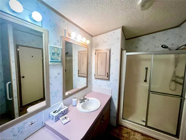 Full bathroom with wallpapered walls, ornamental molding, a textured ceiling, a shower stall, and vanity
