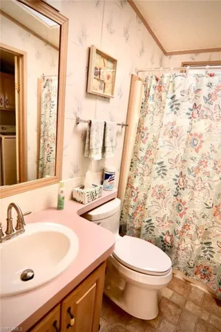 Bathroom featuring wallpapered walls, toilet, vanity, washer / clothes dryer, and curtained shower