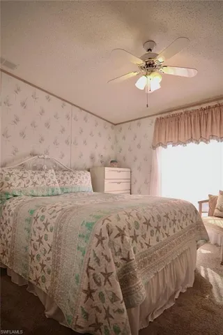 Carpeted bedroom featuring wallpapered walls, a textured ceiling, and ceiling fan