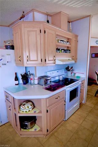 Kitchen featuring electric stove, crown molding, open shelves, light brown cabinetry, and a textured ceiling