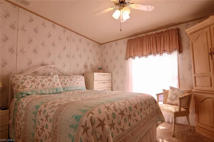 Bedroom featuring wallpapered walls, crown molding, a textured ceiling, carpet flooring, and a ceiling fan