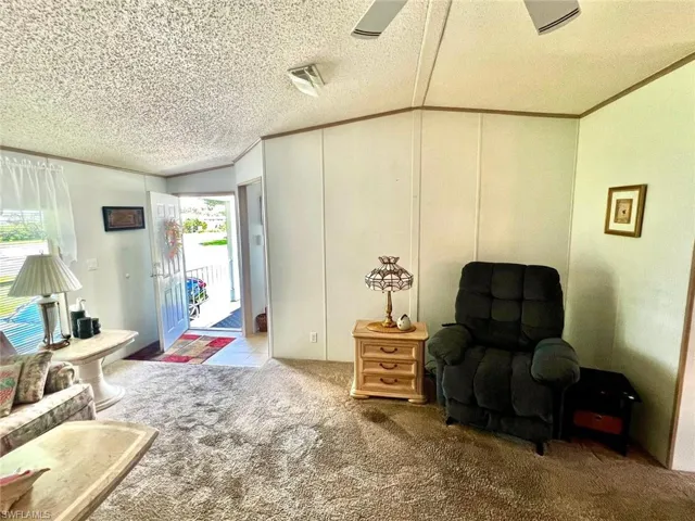 Living area featuring carpet flooring, lofted ceiling, a textured ceiling, and crown molding