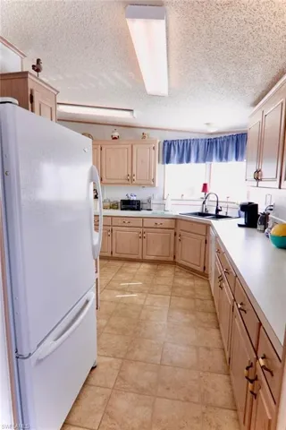 Kitchen featuring freestanding refrigerator, light brown cabinetry, a sink, light countertops, and a textured ceiling