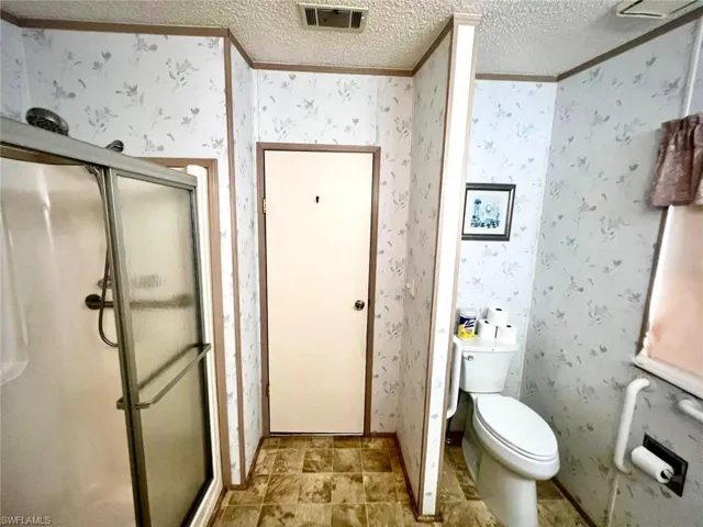 Full bath with crown molding, a shower stall, a textured ceiling, wallpapered walls, and toilet