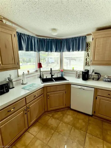 Kitchen featuring dishwasher, a sink, a textured ceiling, plenty of natural light, and light countertops