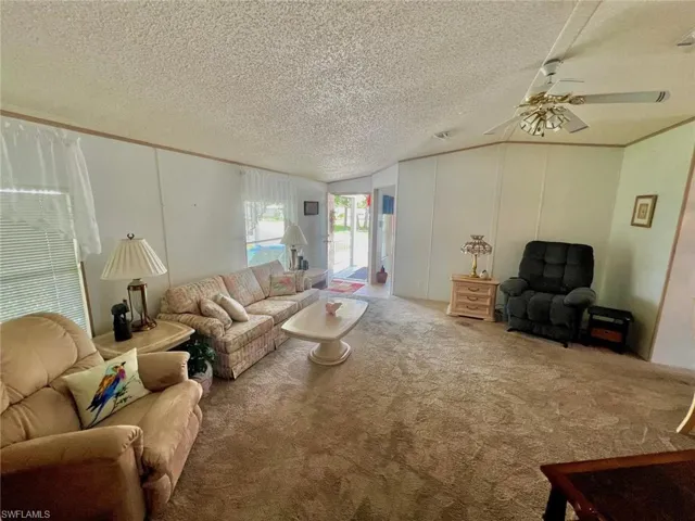 Living area featuring ceiling fan, carpet floors, lofted ceiling, and a textured ceiling