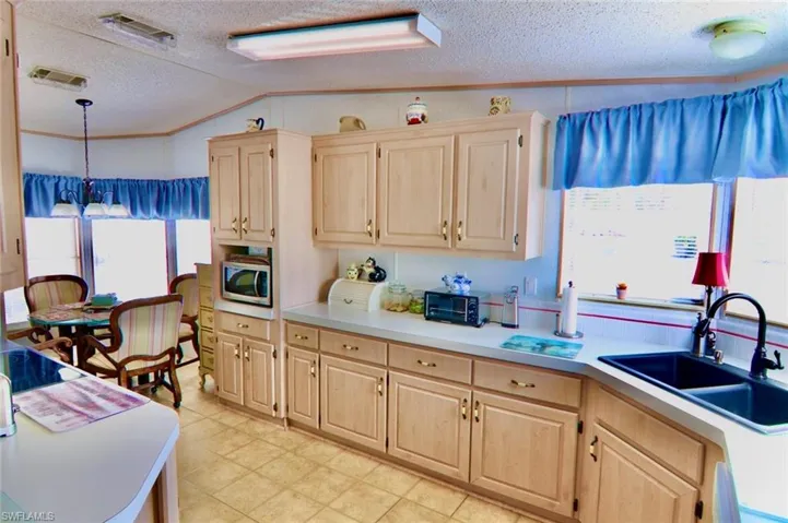 Kitchen featuring stainless steel microwave, light brown cabinetry, a sink, light countertops, and a textured ceiling