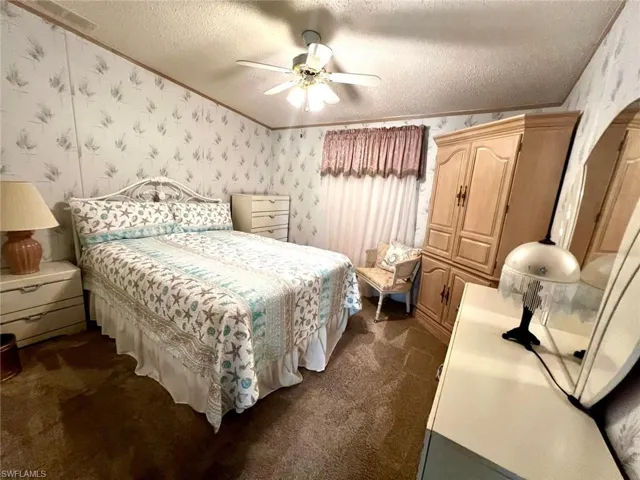 Bedroom with wallpapered walls, a textured ceiling, dark colored carpet, crown molding, and ceiling fan