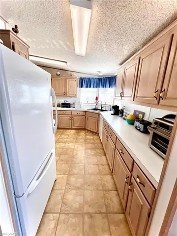 Kitchen with freestanding refrigerator, light brown cabinets, light countertops, a sink, and a textured ceiling