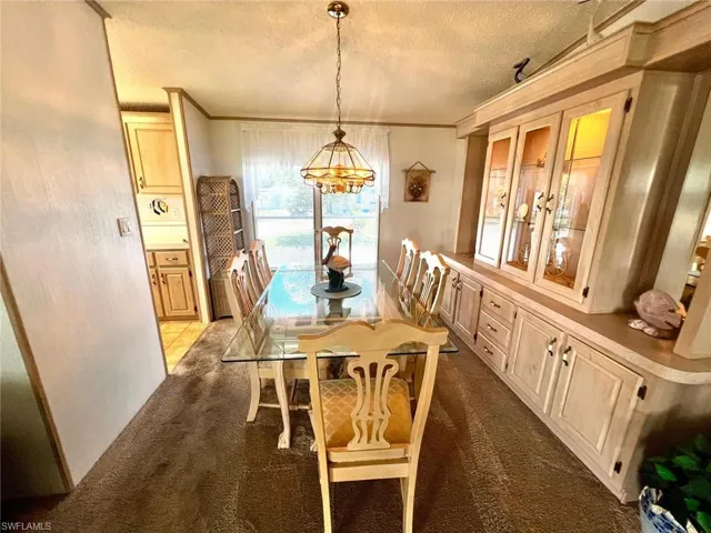 Dining space featuring carpet flooring, a chandelier, a textured ceiling, and ornamental molding