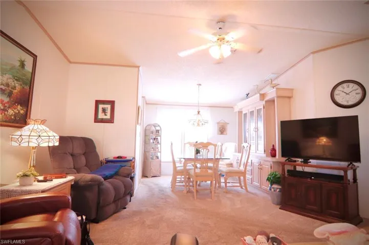 Living room with crown molding, light colored carpet, ceiling fan, and healthy amount of natural light