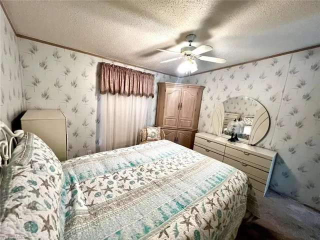 Bedroom featuring crown molding, wallpapered walls, a textured ceiling, and a ceiling fan