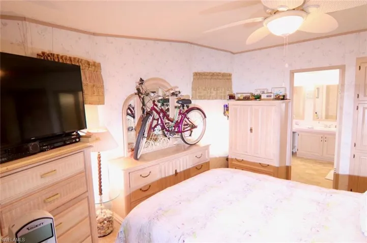 Bedroom with wallpapered walls, ornamental molding, ensuite bath, and ceiling fan