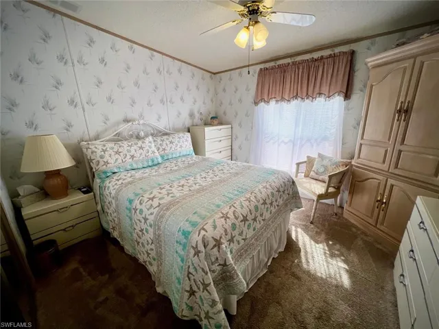 Bedroom with dark carpet, a textured ceiling, ornamental molding, wallpapered walls, and a ceiling fan