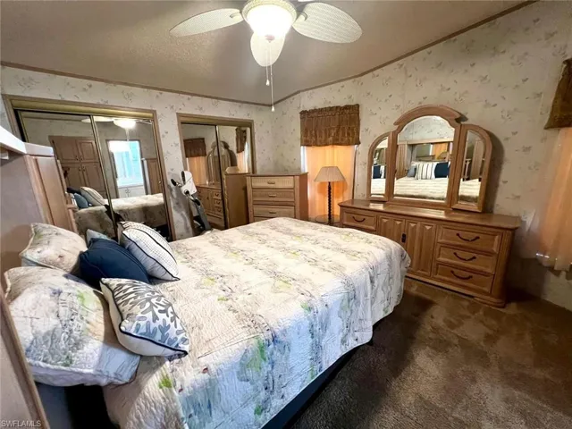 Bedroom featuring wallpapered walls, ornamental molding, lofted ceiling, multiple closets, and dark colored carpet