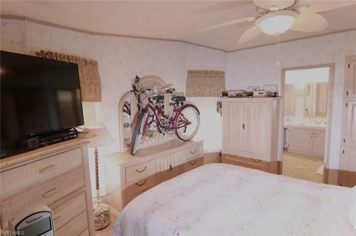 Bedroom with wallpapered walls, crown molding, ensuite bath, and ceiling fan