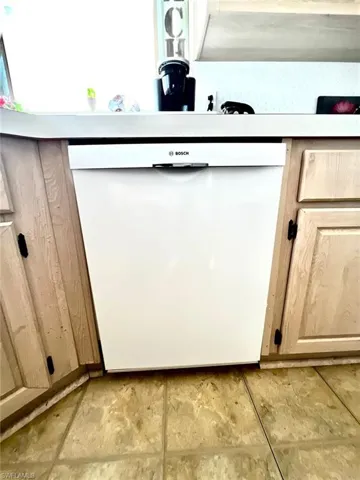 Kitchen view of white dishwasher and light brown cabinetry