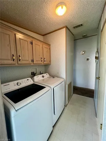 Washroom featuring cabinet space, independent washer and dryer, a textured ceiling, and light tile patterned floors