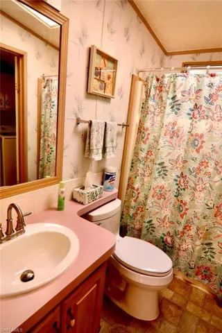 Bathroom with wallpapered walls, toilet, vanity, and curtained shower