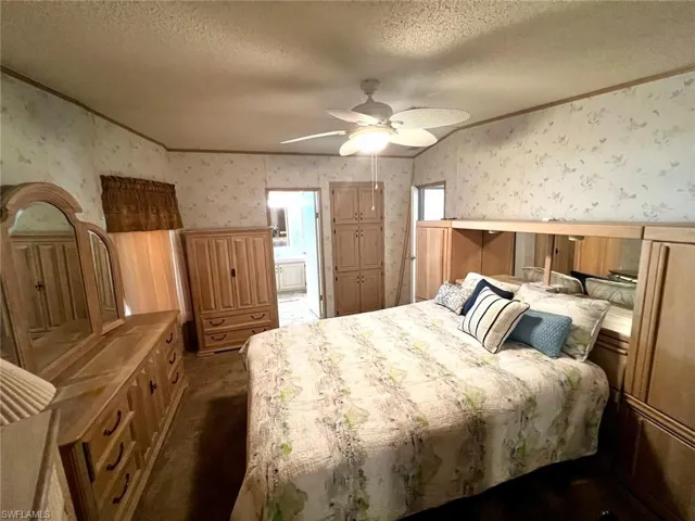 Bedroom with wallpapered walls, crown molding, a textured ceiling, dark colored carpet, and ensuite bath