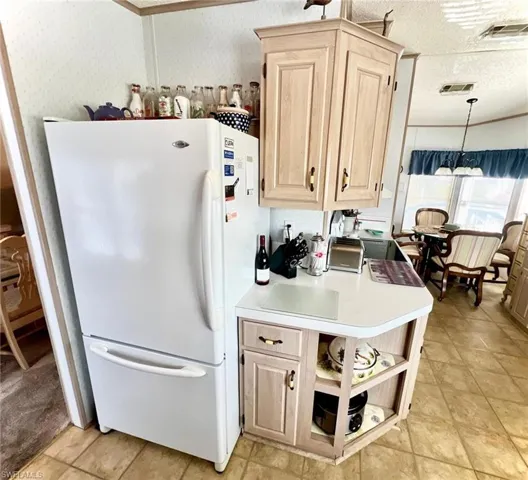Kitchen with freestanding refrigerator, light brown cabinets, wallpapered walls, light countertops, and open shelves