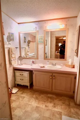 Ensuite bathroom with wallpapered walls, a textured ceiling, crown molding, and vanity