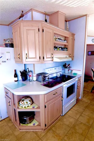 Kitchen with white range with electric stovetop, open shelves, crown molding, light brown cabinetry, and a textured ceiling