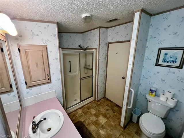 Bathroom featuring wallpapered walls, a textured ceiling, a shower stall, and vanity