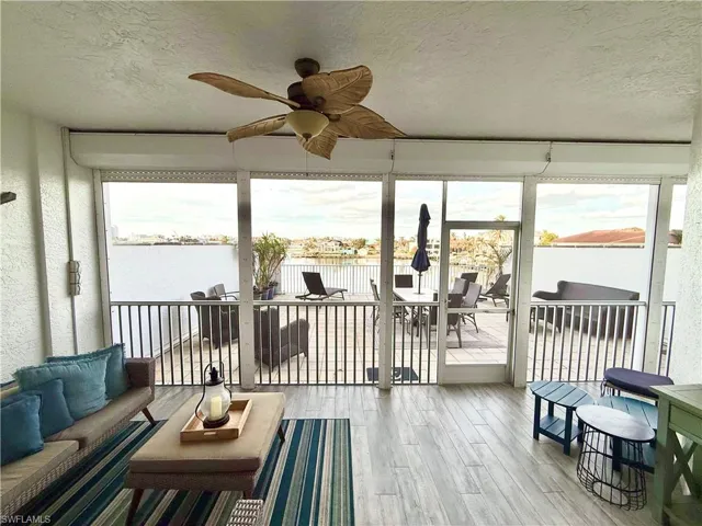 Sunroom / solarium with ceiling fan, a water view, a textured ceiling, wood finished floors, and an outdoor hangout area
