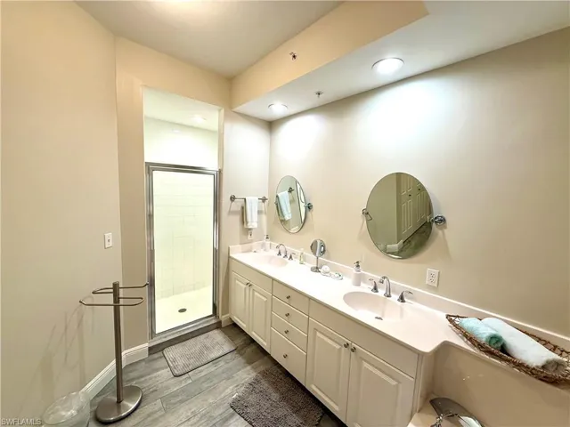 Full bath with a shower stall, light wood-type flooring, and double vanity