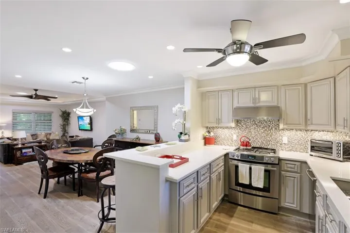 Kitchen featuring stainless steel gas range oven, ceiling fan, under cabinet range hood, open floor plan, and ornamental molding