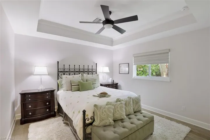 Bedroom featuring a tray ceiling, baseboards, ornamental molding, a ceiling fan, and wood finished floors