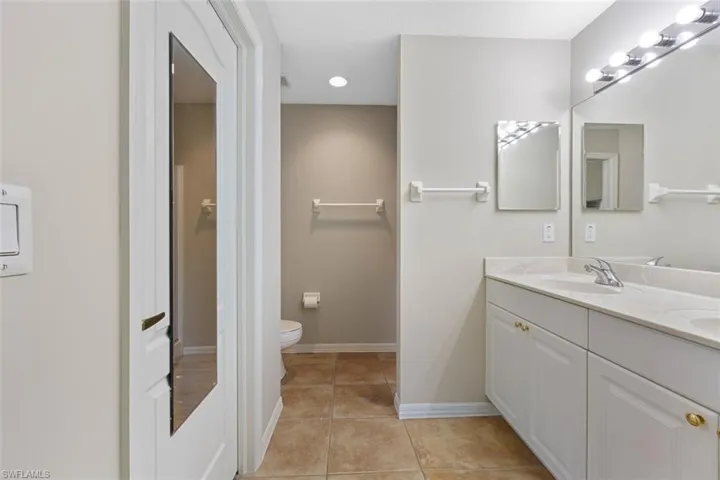 Full bathroom featuring tile patterned flooring, baseboards, toilet, double vanity, and a sink