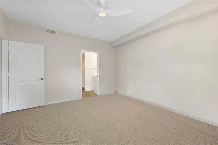 Unfurnished bedroom featuring visible vents, baseboards, ceiling fan, ensuite bathroom, and light colored carpet