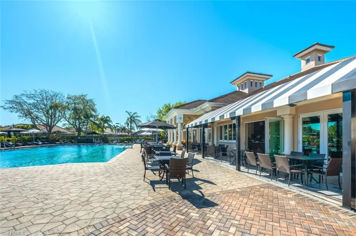 Expansive outdoor patio with patterned paver flooring, shaded seating areas, and a large swimming pool