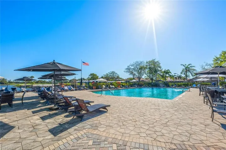 Expansive outdoor pool area featuring a paver patio, multiple lounge chairs, shade umbrellas, and mature landscaping