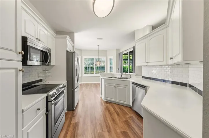 Modern kitchen featuring white cabinetry, stainless steel appliances, white countertops, a subway tile backsplash with a dark accent, and wood-finish flooring
