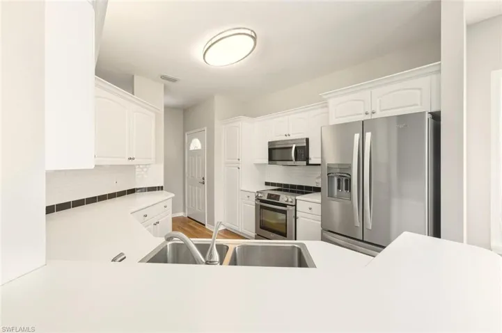 Kitchen featuring white cabinetry, stainless steel appliances, white countertops, and a subway tile backsplash with a black accent border