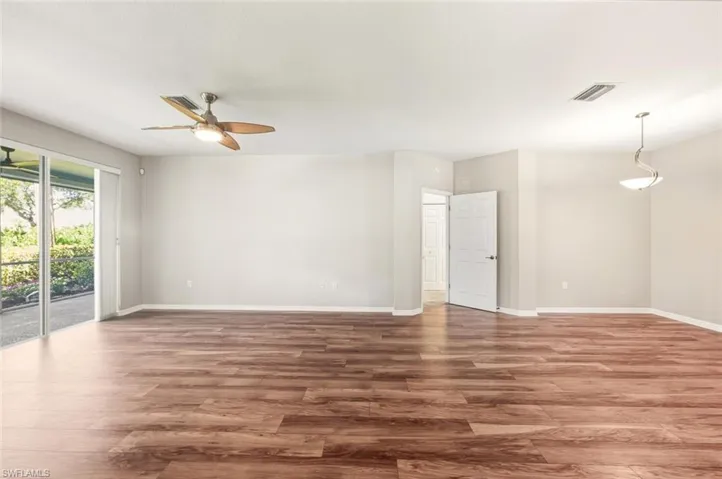 Spacious interior room featuring wood-finish flooring, light-toned walls, and a ceiling fan