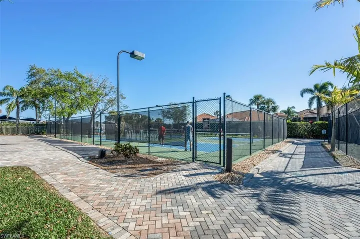Paved brick walkway leading to a fenced tennis court with an overhead light fixture