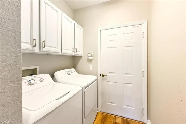 Dedicated utility space featuring overhead white cabinetry with brushed nickel hardware, light neutral wall tones, and wood-finish flooring