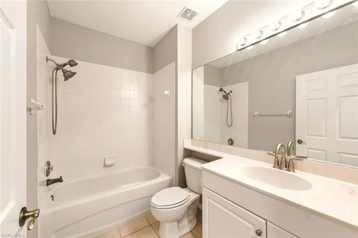 Full bathroom featuring a white tub/shower combination with a bronze-finish shower head, a large vanity mirror, and a white vanity with an integrated sink and brushed nickel faucet