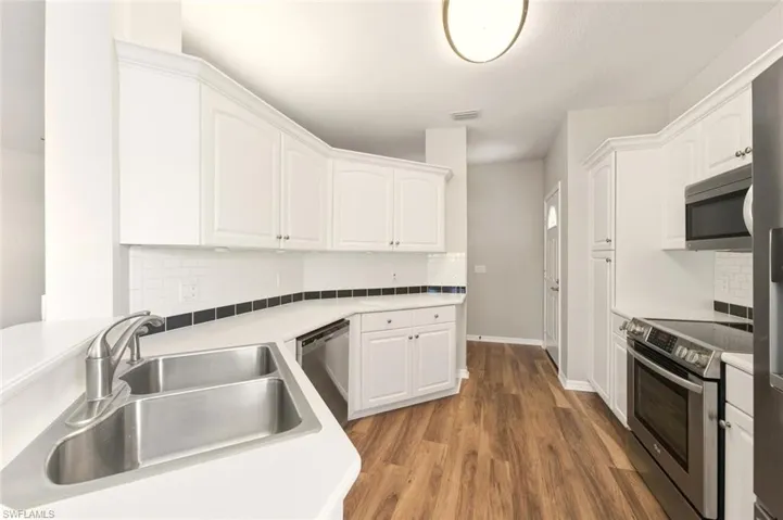 Kitchen featuring white cabinetry, a dual basin stainless steel sink with a brushed nickel faucet, wood-finish flooring, a white subway tile backsplash with a black accent stripe, and stainless steel appliances